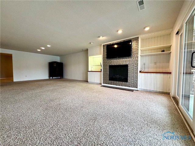 unfurnished living room featuring a textured ceiling, a fireplace, visible vents, and carpet