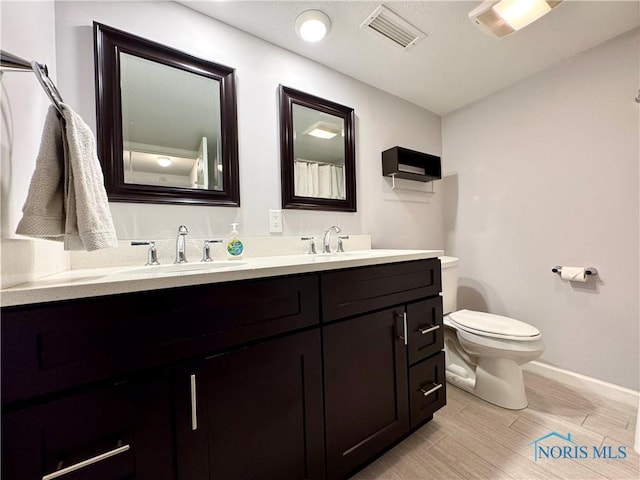 bathroom featuring toilet, wood finished floors, a sink, and visible vents