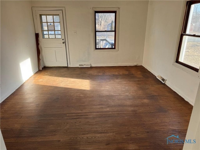 spare room with dark wood-type flooring, plenty of natural light, and visible vents