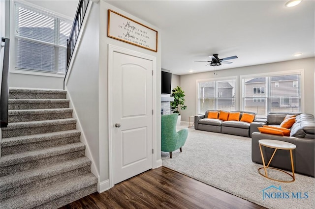 living area featuring dark wood-style flooring, a fireplace, a ceiling fan, baseboards, and stairs