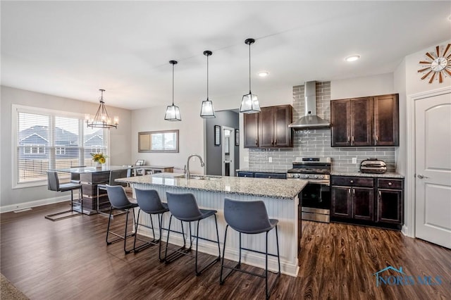 kitchen with stainless steel range with gas cooktop, wall chimney exhaust hood, dark wood-type flooring, a sink, and a kitchen breakfast bar