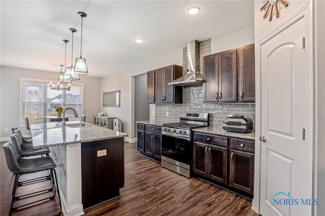 kitchen with dark wood-type flooring, a sink, backsplash, wall chimney exhaust hood, and gas stove