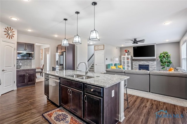 kitchen featuring a fireplace, a breakfast bar area, appliances with stainless steel finishes, dark wood-type flooring, and a sink