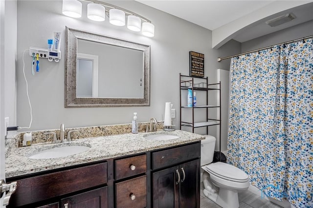 bathroom featuring a shower with shower curtain, a sink, toilet, and double vanity