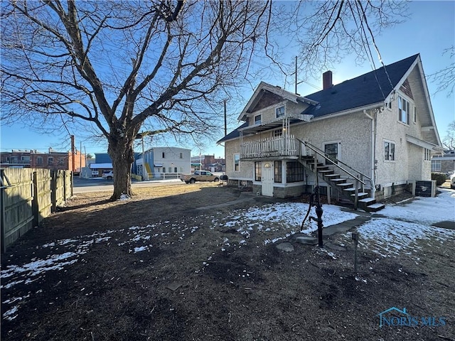 rear view of property with stairs, a chimney, fence, and stucco siding