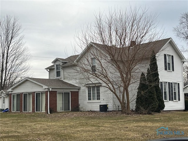 rear view of house featuring a yard, brick siding, and roof with shingles