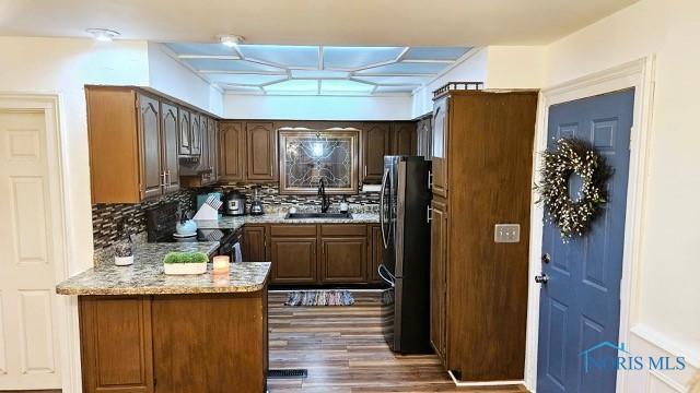 kitchen with stainless steel appliances, a peninsula, a sink, backsplash, and dark wood finished floors