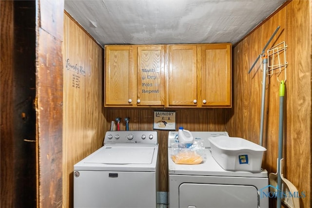 washroom featuring washing machine and dryer, cabinet space, and wood walls