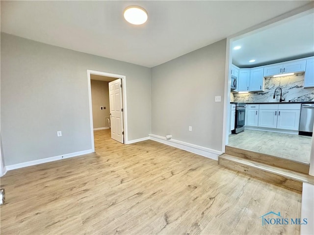 unfurnished living room featuring light wood finished floors, recessed lighting, a sink, and baseboards