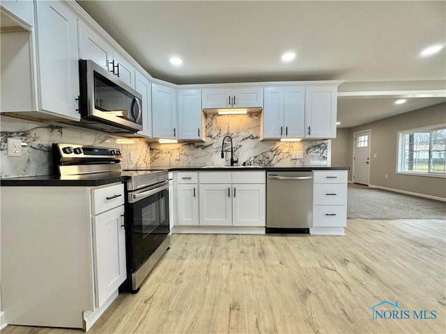 kitchen featuring appliances with stainless steel finishes, dark countertops, light wood-style floors, and a sink