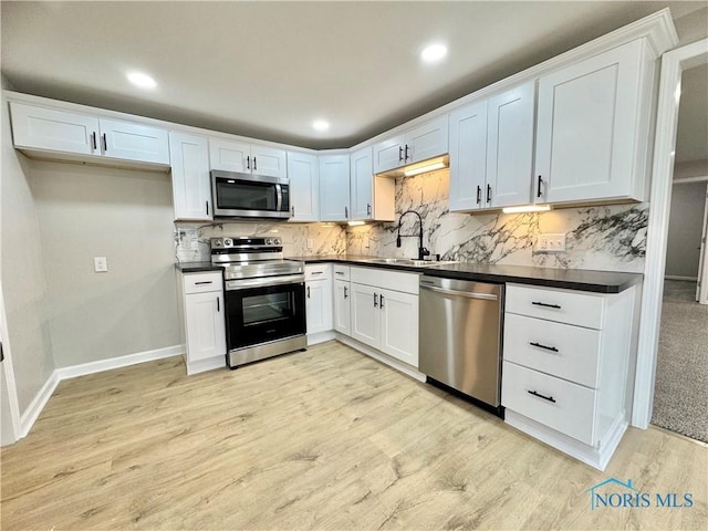 kitchen with appliances with stainless steel finishes, dark countertops, light wood-type flooring, and a sink