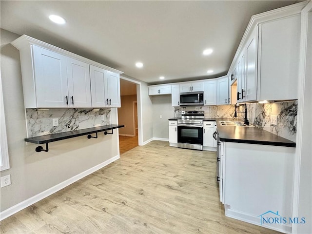 kitchen with white cabinets, dark countertops, stainless steel appliances, light wood-style floors, and a sink