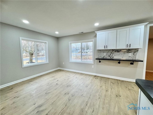 interior space with baseboards, dark countertops, white cabinetry, and light wood-style floors