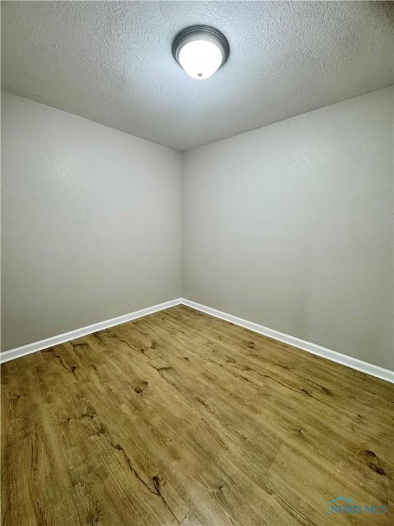 spare room with a textured ceiling, wood finished floors, and baseboards