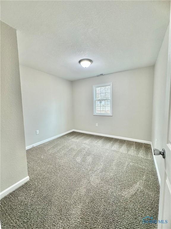 carpeted spare room with visible vents, baseboards, and a textured ceiling