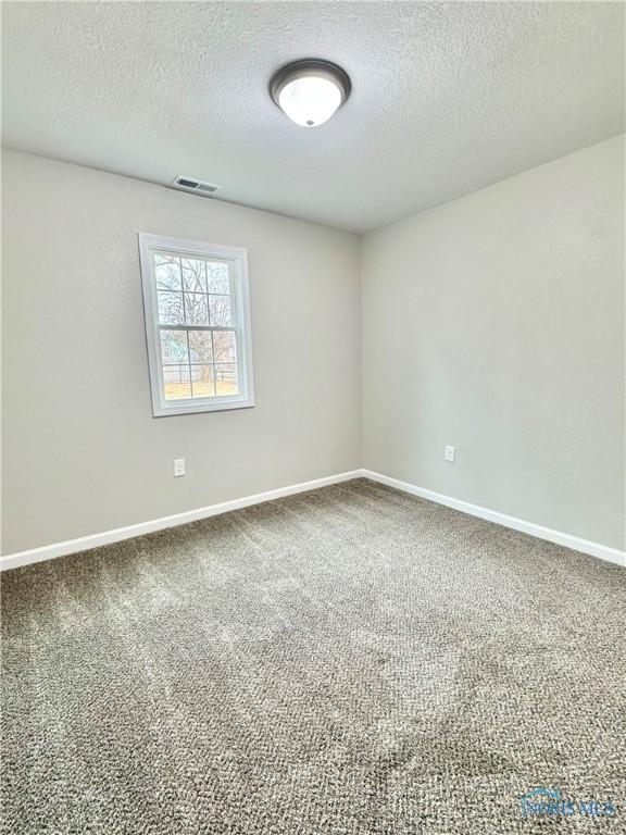 carpeted empty room featuring visible vents, a textured ceiling, and baseboards