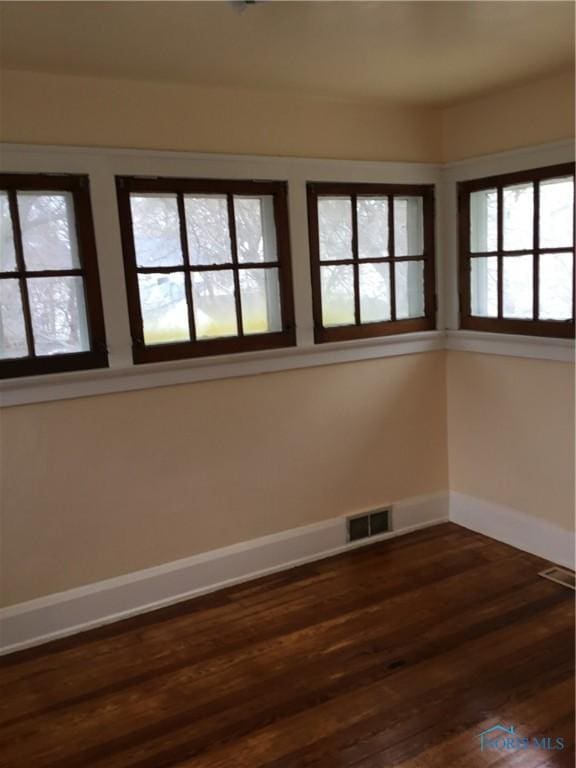 unfurnished room featuring dark wood finished floors, visible vents, and baseboards