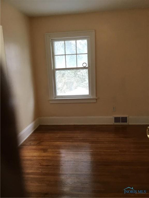 spare room with dark wood-type flooring, visible vents, and baseboards