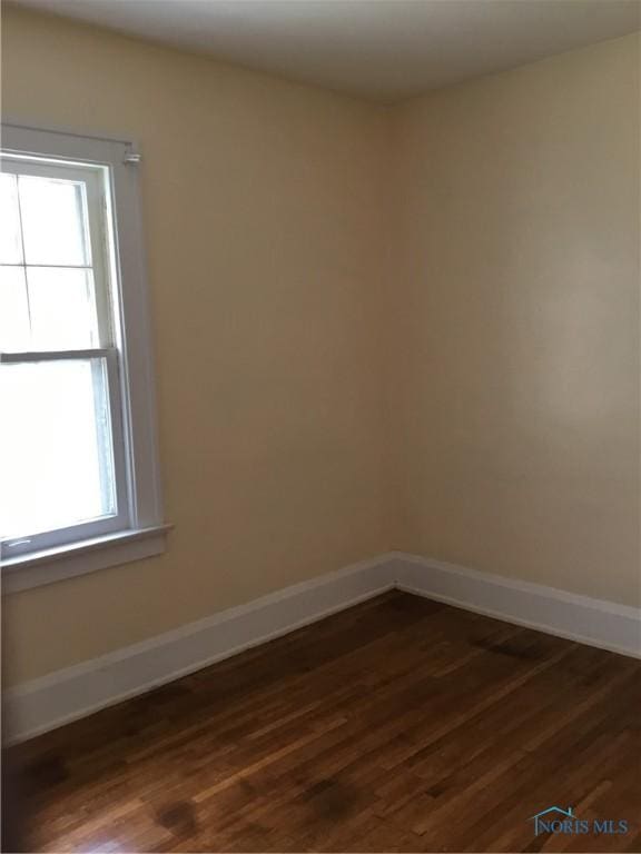 spare room with baseboards, dark wood-type flooring, and a healthy amount of sunlight