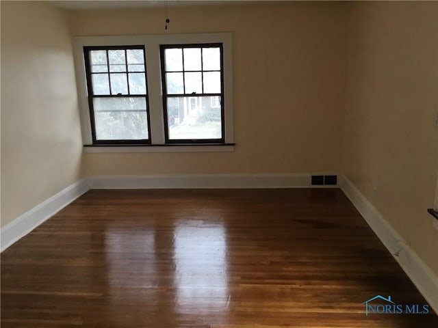 spare room featuring wood finished floors, visible vents, and baseboards