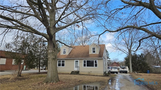 cape cod-style house featuring roof with shingles, driveway, and entry steps