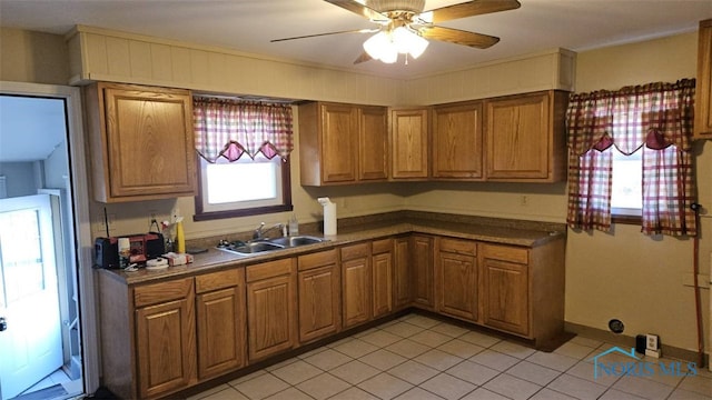 kitchen with a sink, a ceiling fan, light tile patterned flooring, and brown cabinetry