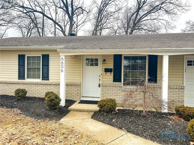 entrance to property featuring brick siding, a porch, and a shingled roof