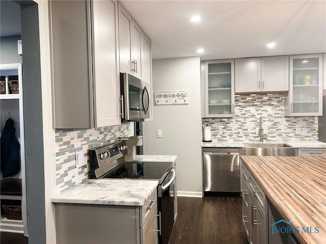 kitchen with appliances with stainless steel finishes, gray cabinets, a sink, and dark wood finished floors