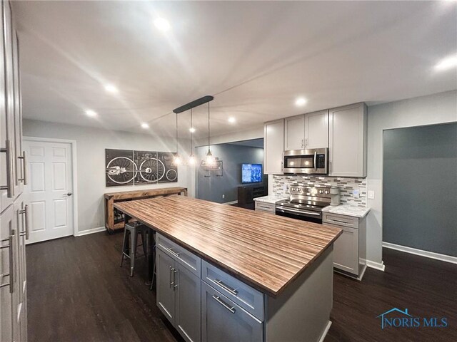 kitchen with gray cabinetry, stainless steel appliances, dark wood-style flooring, wooden counters, and decorative backsplash