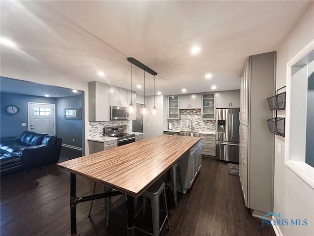 kitchen with decorative backsplash, butcher block countertops, glass insert cabinets, appliances with stainless steel finishes, and dark wood-style flooring