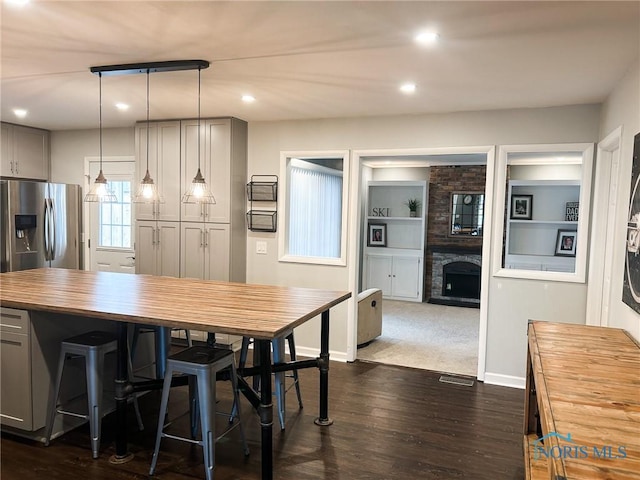 kitchen with stainless steel fridge with ice dispenser, dark wood-style flooring, gray cabinetry, a fireplace, and wooden counters