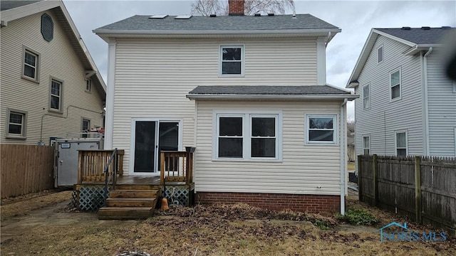 rear view of house with a deck, a shingled roof, a chimney, and fence