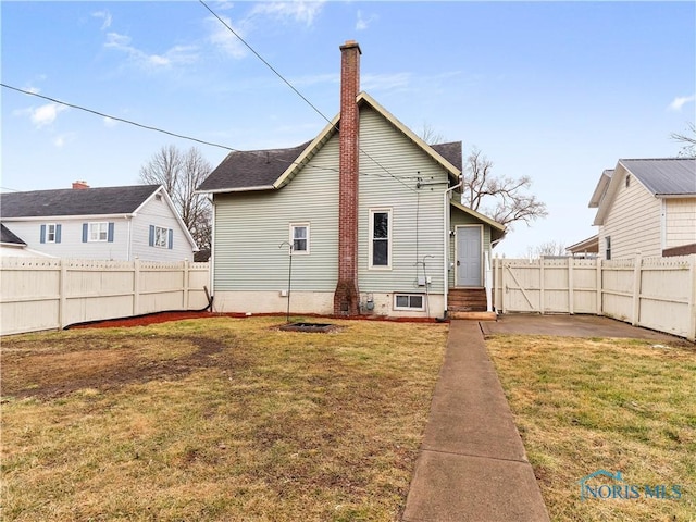 rear view of property featuring entry steps, a fenced backyard, a chimney, a yard, and a patio area