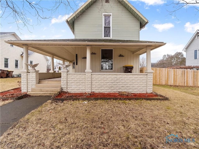 farmhouse-style home featuring covered porch, fence, board and batten siding, and a front yard