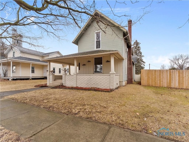 view of front of property with covered porch, a chimney, a front yard, and fence