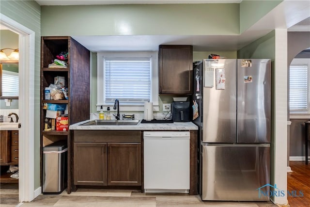 kitchen with white dishwasher, dark brown cabinets, a sink, and freestanding refrigerator