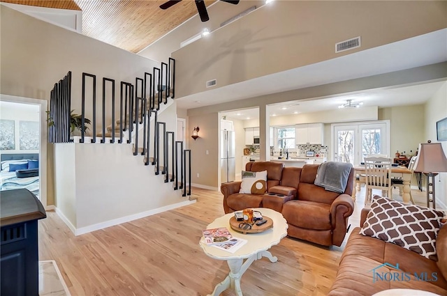 living room with visible vents, stairway, a high ceiling, and light wood-style floors