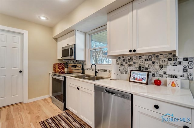 kitchen with decorative backsplash, light wood-style flooring, appliances with stainless steel finishes, white cabinetry, and a sink