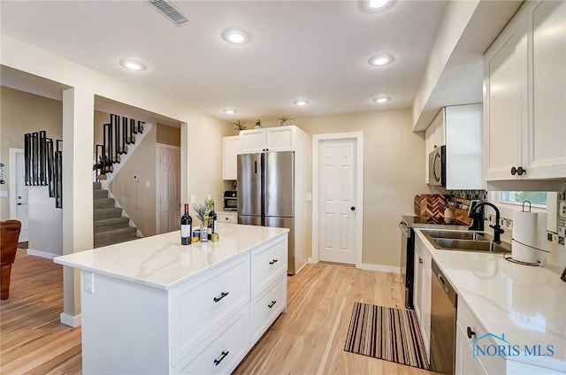 kitchen with light wood finished floors, visible vents, appliances with stainless steel finishes, white cabinets, and a sink