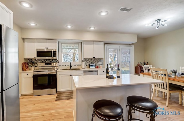 kitchen with light wood finished floors, backsplash, a breakfast bar, stainless steel appliances, and a sink