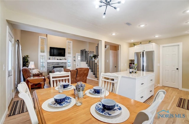 dining area featuring light wood finished floors, visible vents, stairs, a fireplace, and a notable chandelier