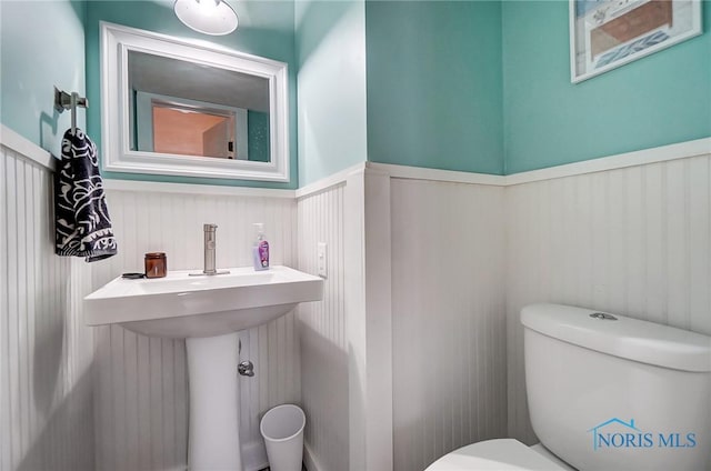 half bathroom featuring a sink, toilet, and wainscoting