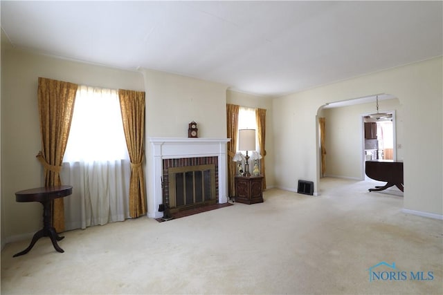 living room featuring arched walkways, carpet flooring, a fireplace, and baseboards