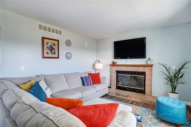 living room with a brick fireplace, visible vents, and wood finished floors