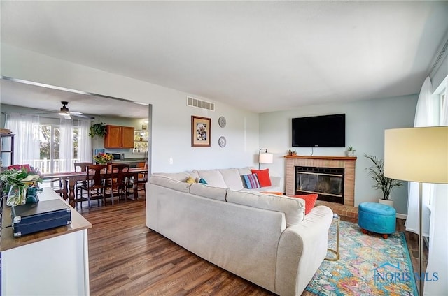 living area featuring ceiling fan, visible vents, a fireplace, and wood finished floors