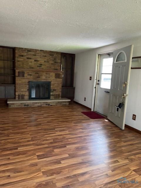 unfurnished living room with a textured ceiling, a fireplace, baseboards, and wood finished floors