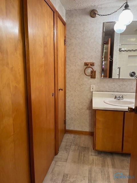 bathroom with a textured ceiling, wood finished floors, vanity, and baseboards