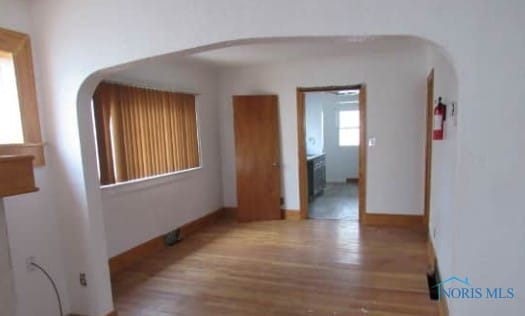 empty room with arched walkways, baseboards, and wood finished floors