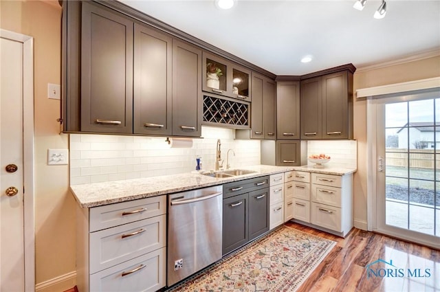 kitchen featuring tasteful backsplash, stainless steel dishwasher, a sink, and light wood-style floors