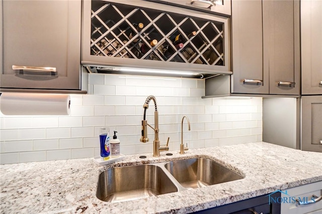 kitchen featuring tasteful backsplash, light stone counters, a sink, and gray cabinetry